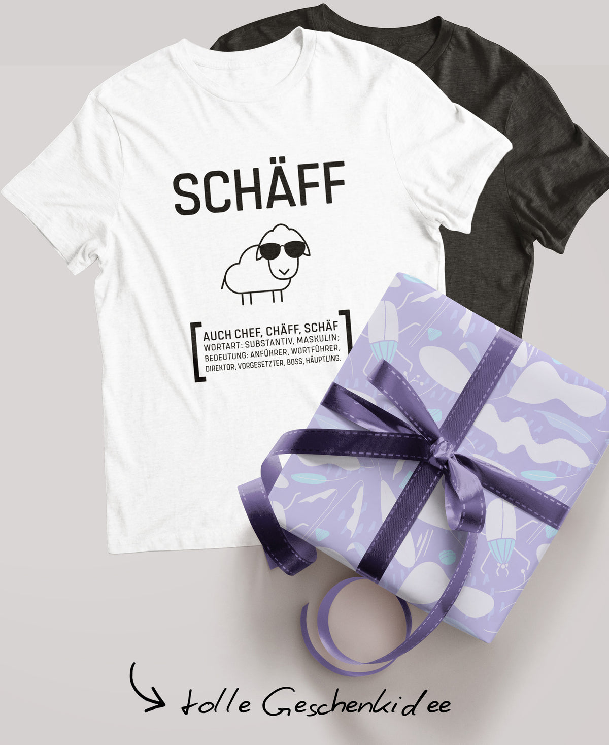 Schwarzes und weisses Schäff T-Shirt; daneben ein verpacktes Geschenk mit lila Schleife und der Schriftzug ‚tolle Geschenkidee‘.