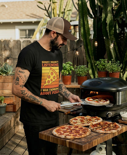 Mann mit Schäff Pizza Retro Trucker Cap  und Schäff Pizza T-Shirt beim Pizzabacken in modernem Outdoor Pizzaofen im Garten.