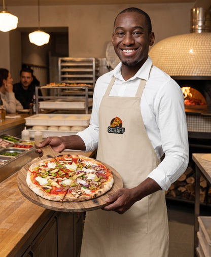 Pizzabäcker mit naturfarbener SCHÄFF Pizzabäcker Schürze zeigt leckere frisch gebackene Pizza auf einem Holzbrett.