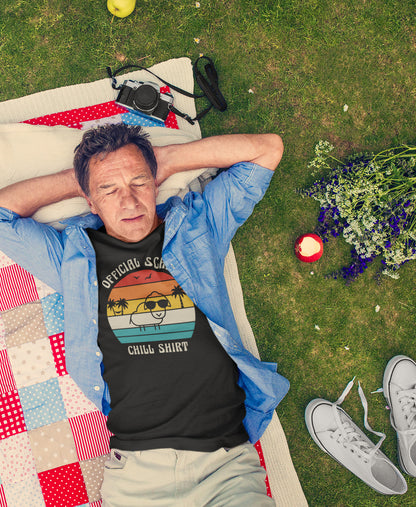 Mann liegt entspannt auf Picknickdecke und trägt SCHÄFF – Official Chill Shirt Bio T-Shirt in Schwarz, mit lustigem Schaf mit Sonnenbrille, Palmen und Retro Streifen in Sunset Farben
