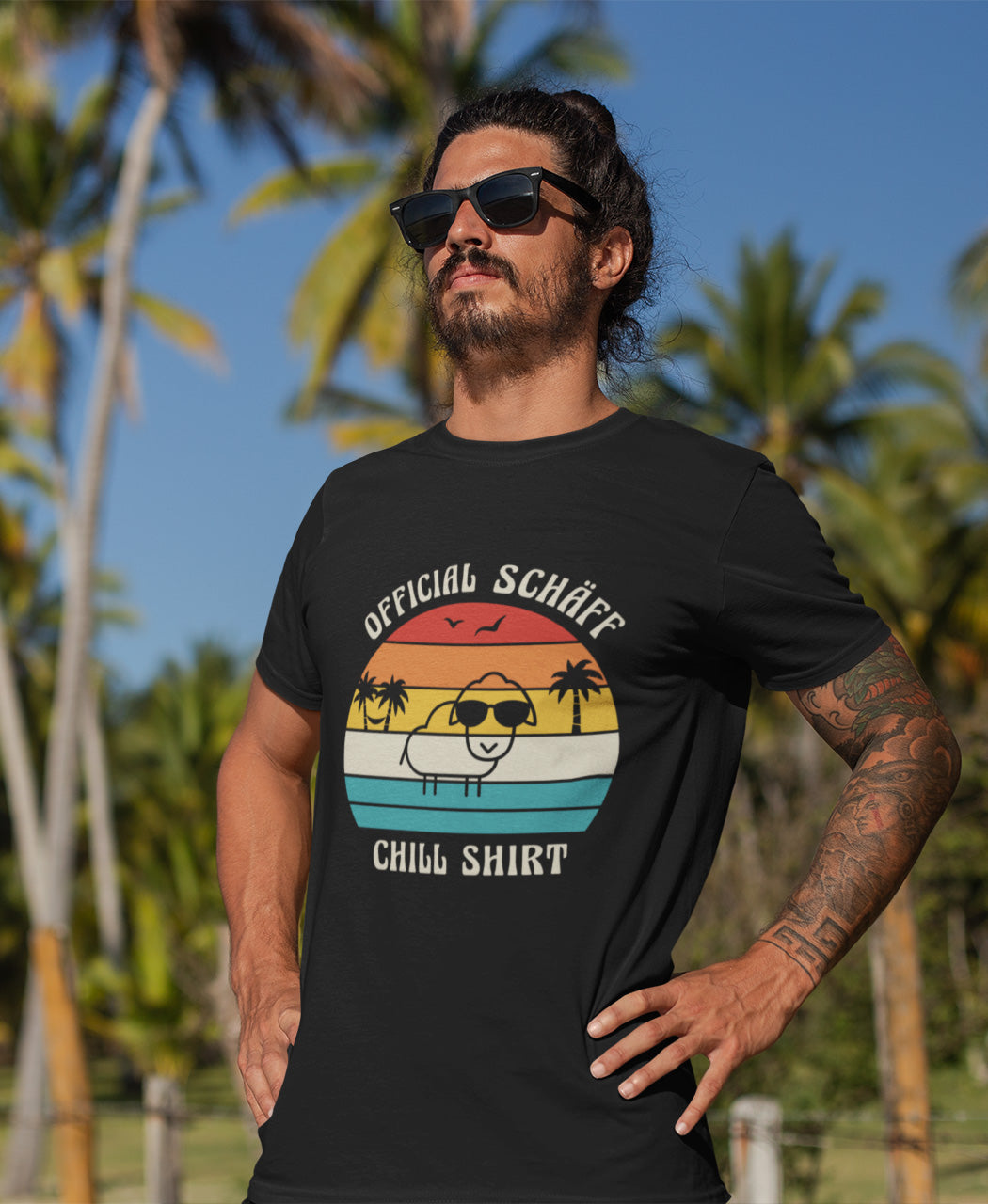 Nahaufnahme Mann trägt SCHÄFF – Official Chill Shirt  Bio T-Shirt in Schwarz, mit lustigem Schaf mit Sonnenbrille, Palmen und Retro Streifen in Sunset Farben
