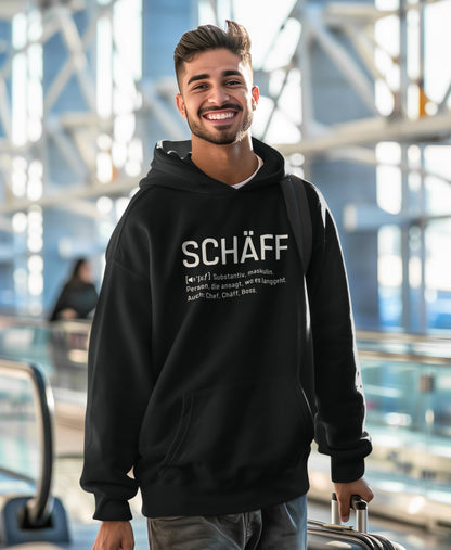 Lachender Mann am Flughafen trägt SCHÄFF – Chef Definition Bio-Hoodie in Schwarz