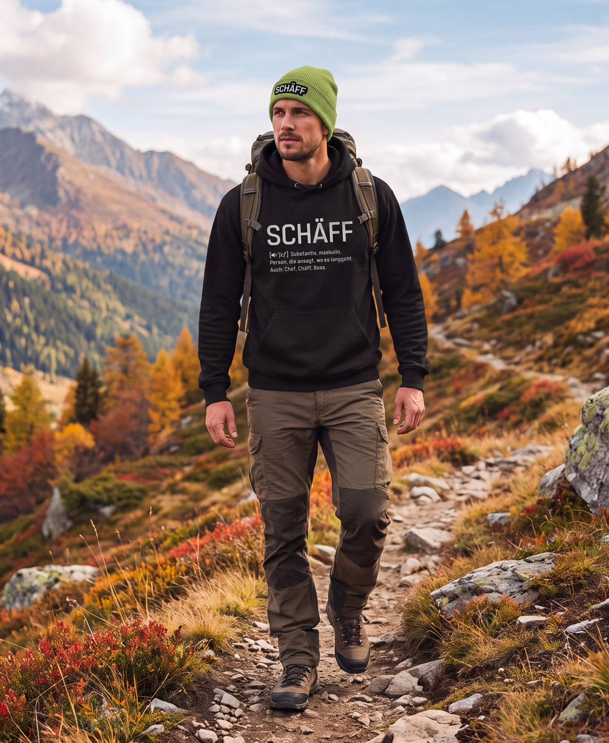 Mann in den Bergen beim Wandern mit  SCHÄFF Beanie – Bio-Baumwolle Mütze in Grün und SCHÄFF – Chef Definition Bio-Hoodie in Schwarz