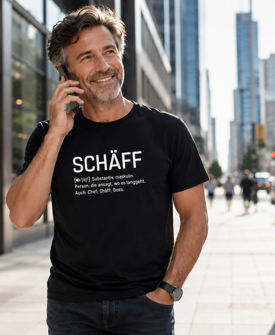 Mann in schwarzem SCHÄFF Chef Definition Bio T-Shirt mit minimalistischem weißem Schriftzug, unterwegs in einer modernen Großstadt.
