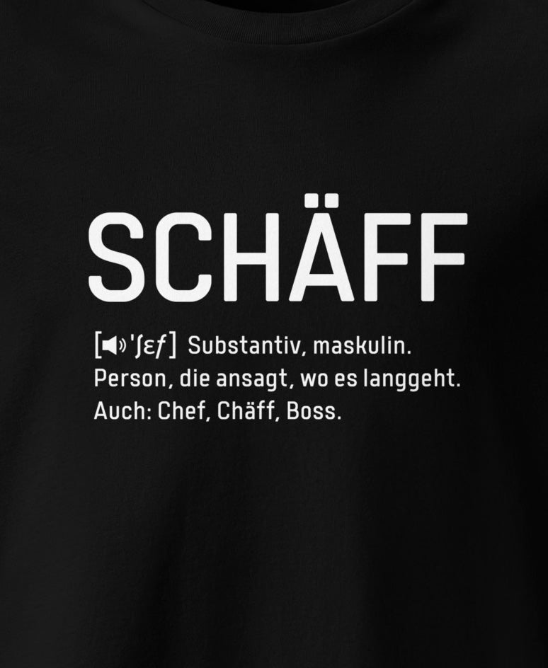Ausschnitt eines Schwarzen T-Shirt mit weissem Frontaufdruck im Wörterbuch-Stil: SCHÄFF – Substantiv, maskulin. Person, die ansagt, wo es langgeht. Auch: Chef, Chäff, Boss.