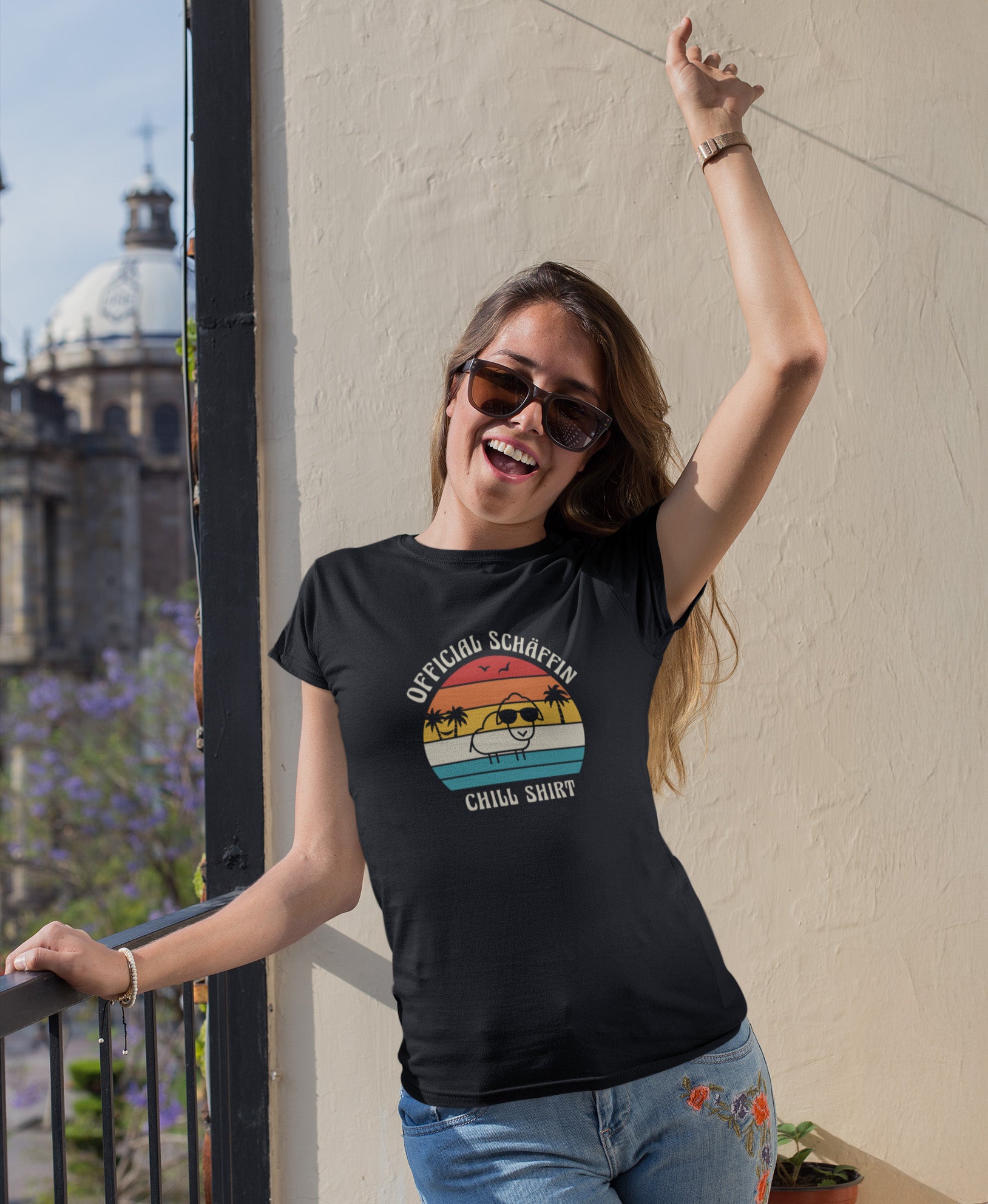 Frau auf Balkon trägt SCHÄFFIN – Official Chill Shirt mit Urlaubsmotiv & Sonnenbrille Bio T-Shirt in Schwarz