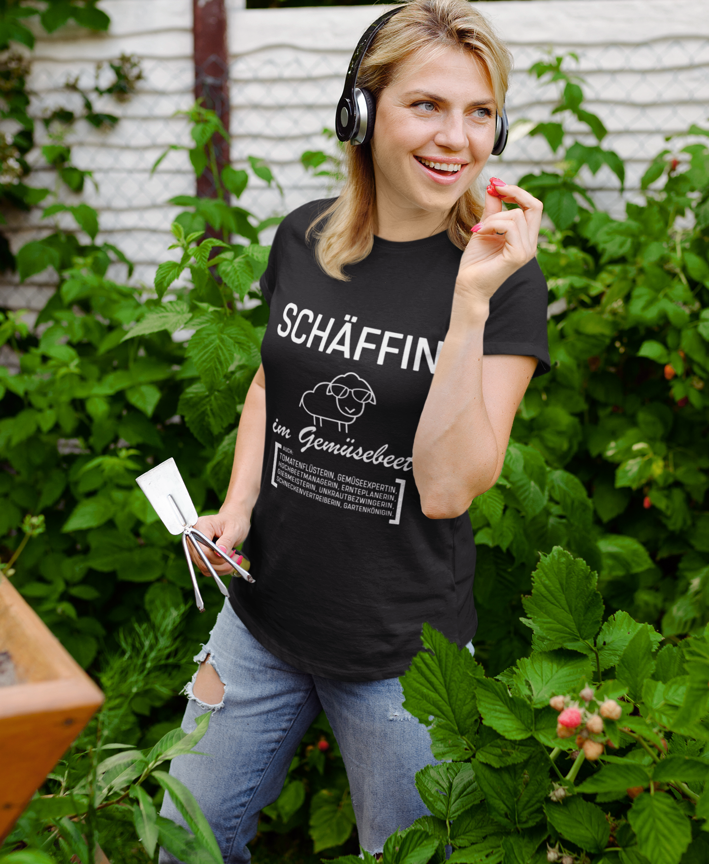 Frau trägt schwarzes SCHÄFFIN T-Shirt im Garten beim Pflanzen. Lustiges Gärtnerin T-Shirt mit Gemüsebeet-Motiv.