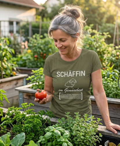Gärtnerin trägt khakigrünes SCHÄFFIN T-Shirt im Gemüsebeet und hält eine reife Tomate in der Hand.