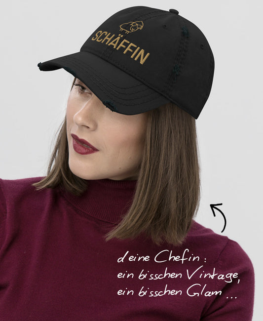 Frau mit schwarzem Schäffin Dad-Hat im Used-Look und Hinweis: ‚deine Chefin: ein bisschen Vintage, ein bisschen Glam…’