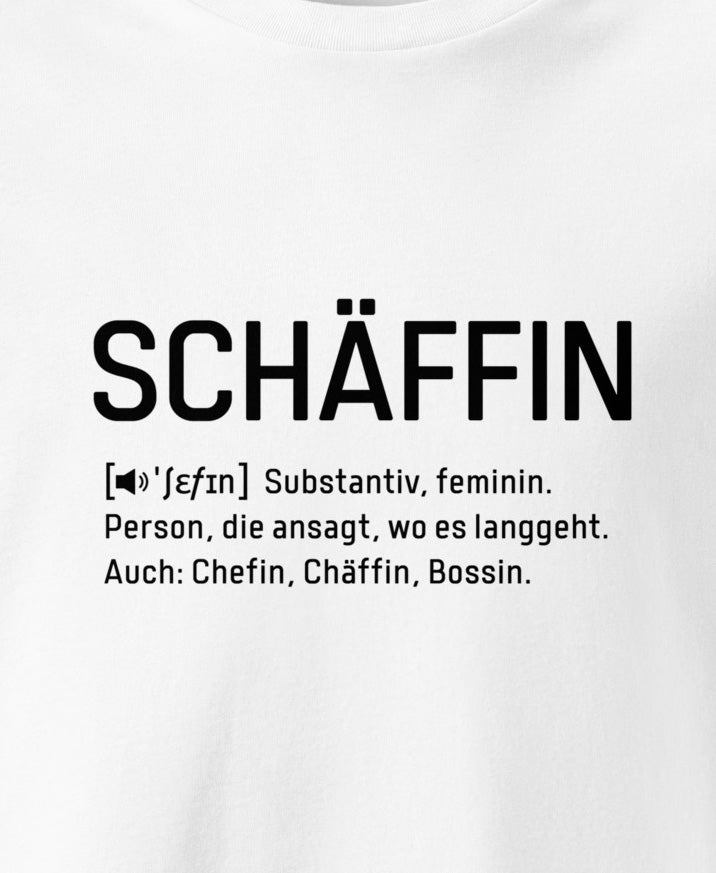 Weisses T-Shirt mit schwarzem Frontaufdruck (Close-up) im Wörterbuch-Stil: SCHÄFFIN – Substantiv, feminin. Person, die ansagt, wo es langgeht. Auch: Chefin, Chäffin, Bossin.