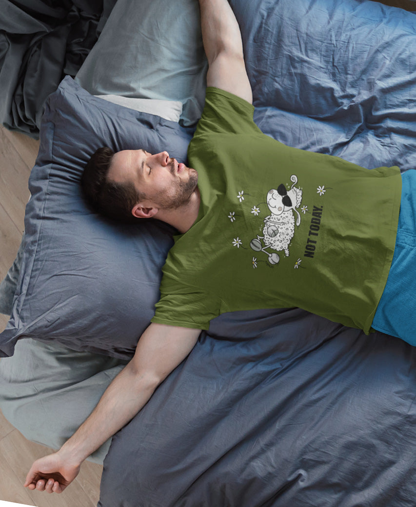 Mann liegt entspannt auf Bett und trägt SCHÄFF Not Today Schaf Bio T-Shirt mit Comic Schaf und Sonnenbrille in Khakigrün