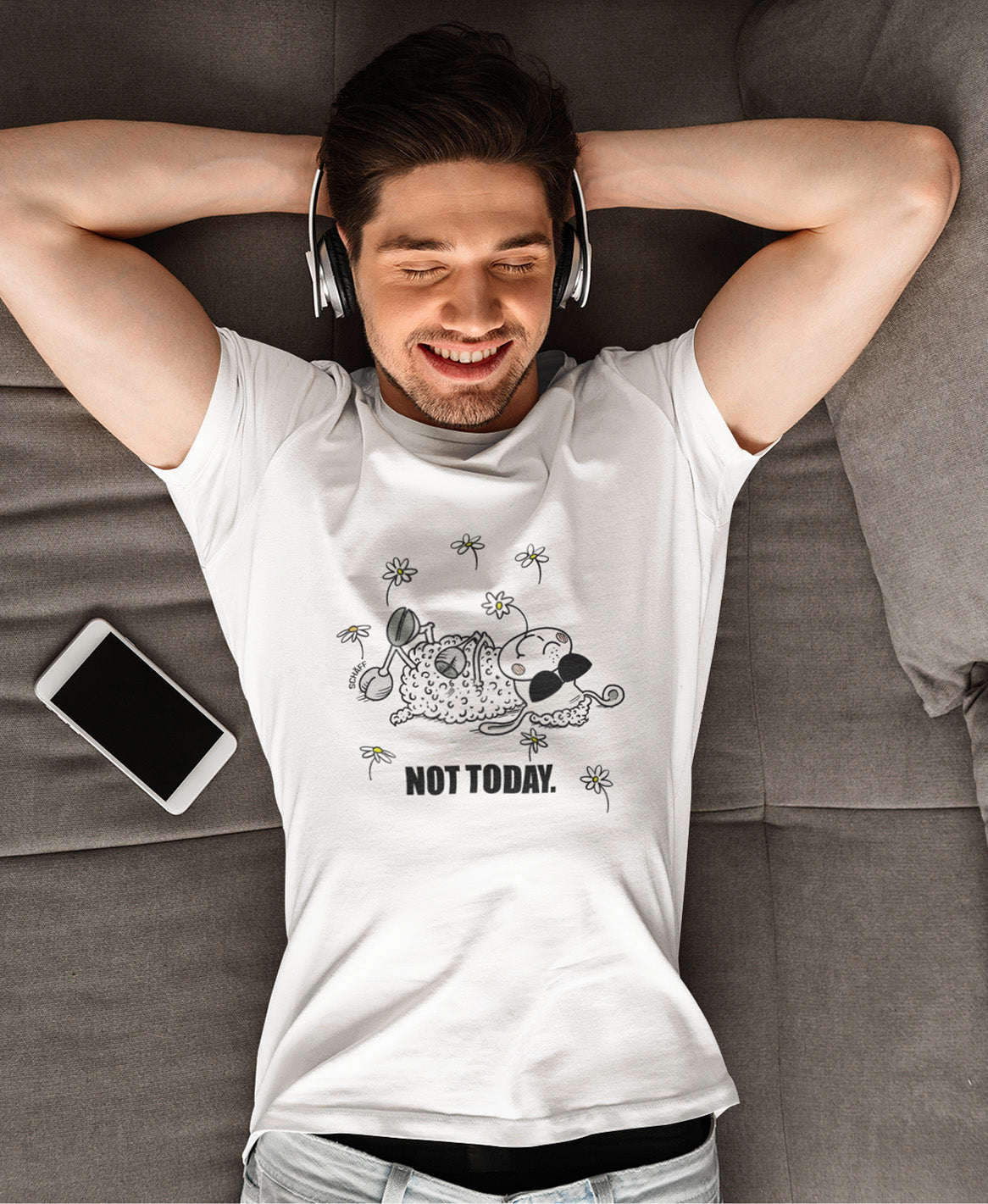 Mann liegt entspannt auf Sofa mit Kopfhörern und trägt SCHÄFF Not Today Schaf Bio T-Shirt mit Comic Schaf und Sonnenbrille in Weiss
