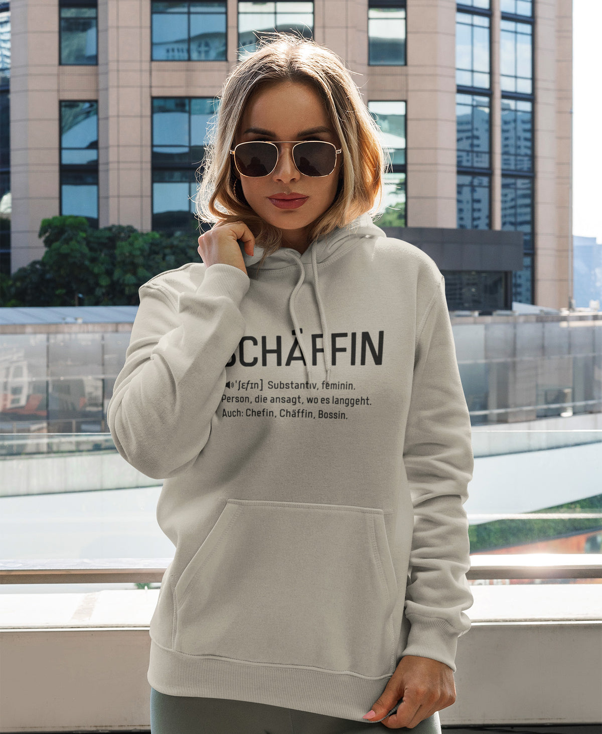 Frau vor Geschäftshaus mit kuscheligem SCHÄFFIN – Chefin Definition Bio-Hoodie in Farbe Desert Dust